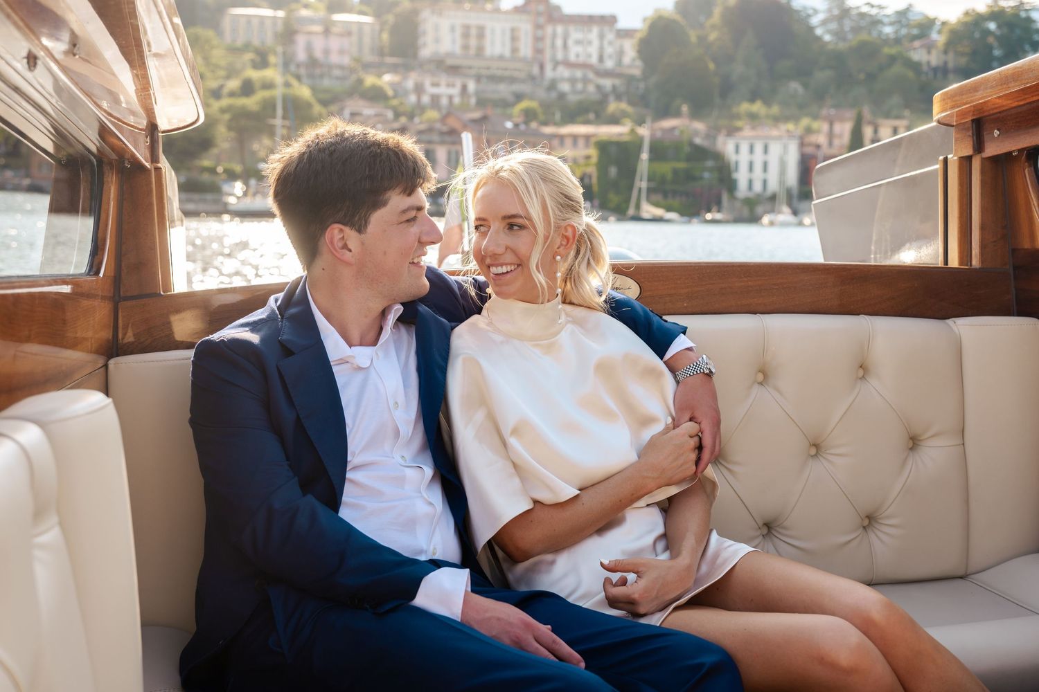 Couple sits close together on a boat's cream leather bench seating while enjoying a scenic waterfront view.