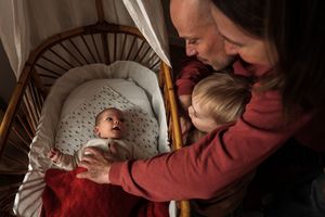 A person in a burgundy sweater cradles and feeds a small baby wrapped in a gray blanket.