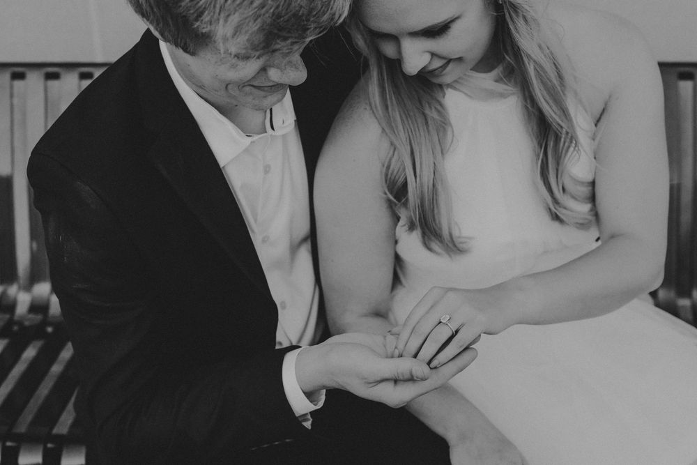 Black and white intimate moment showing two people examining a ring together in a tender engagement scene.