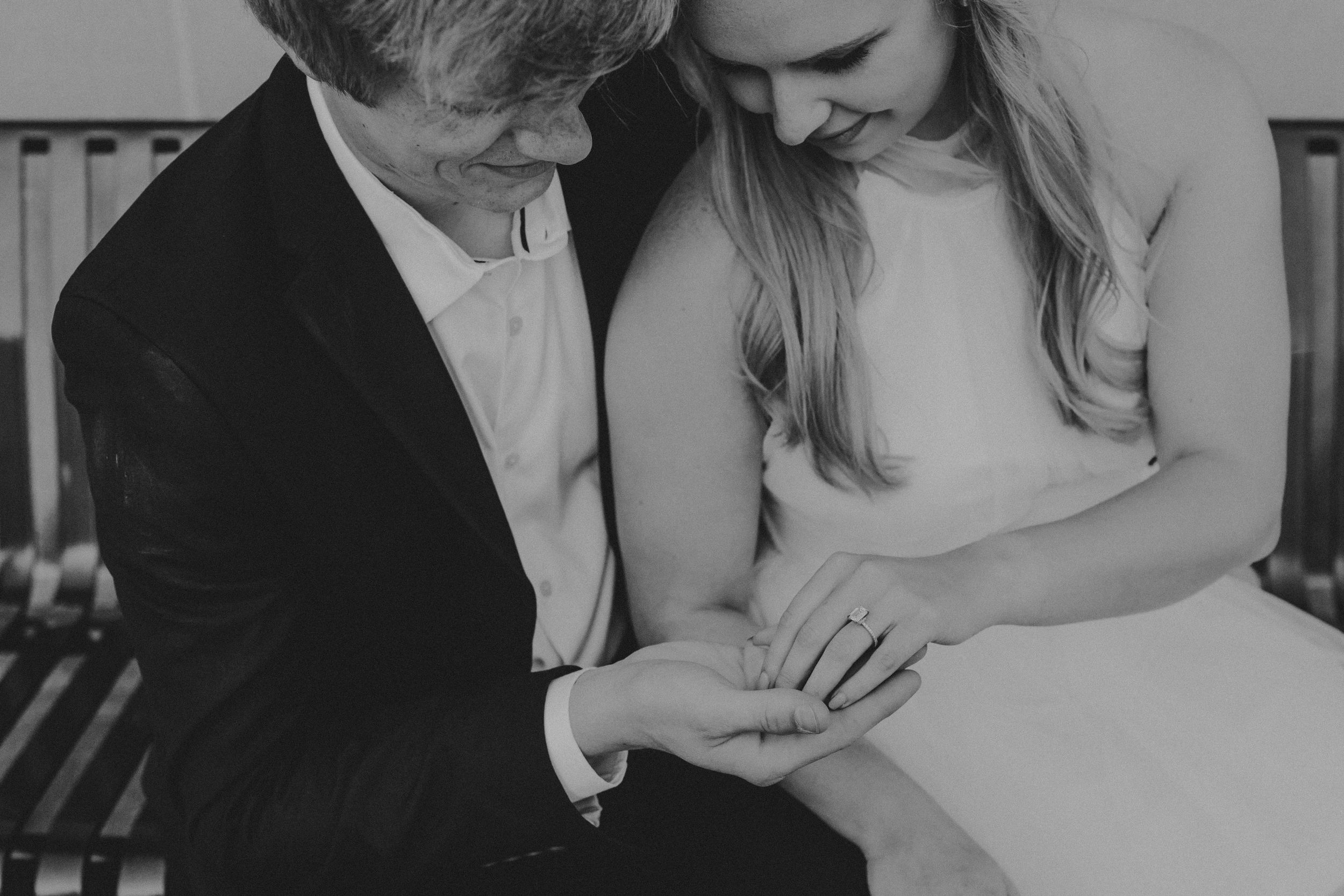 Black and white intimate moment showing two people examining a ring together in a tender engagement scene.