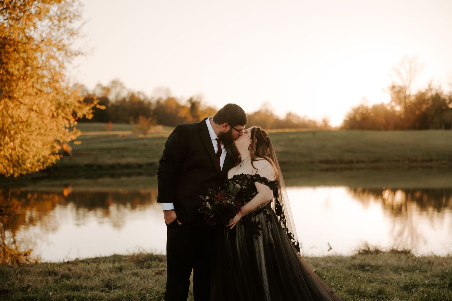 Silhouetted couple shares romantic moment at sunset by tranquil lake with golden light reflecting on water.