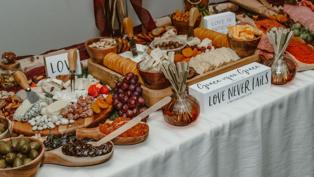 Elegant wedding charcuterie grazing table with cheeses, fruits, meats, and a Love Never Fails sign.