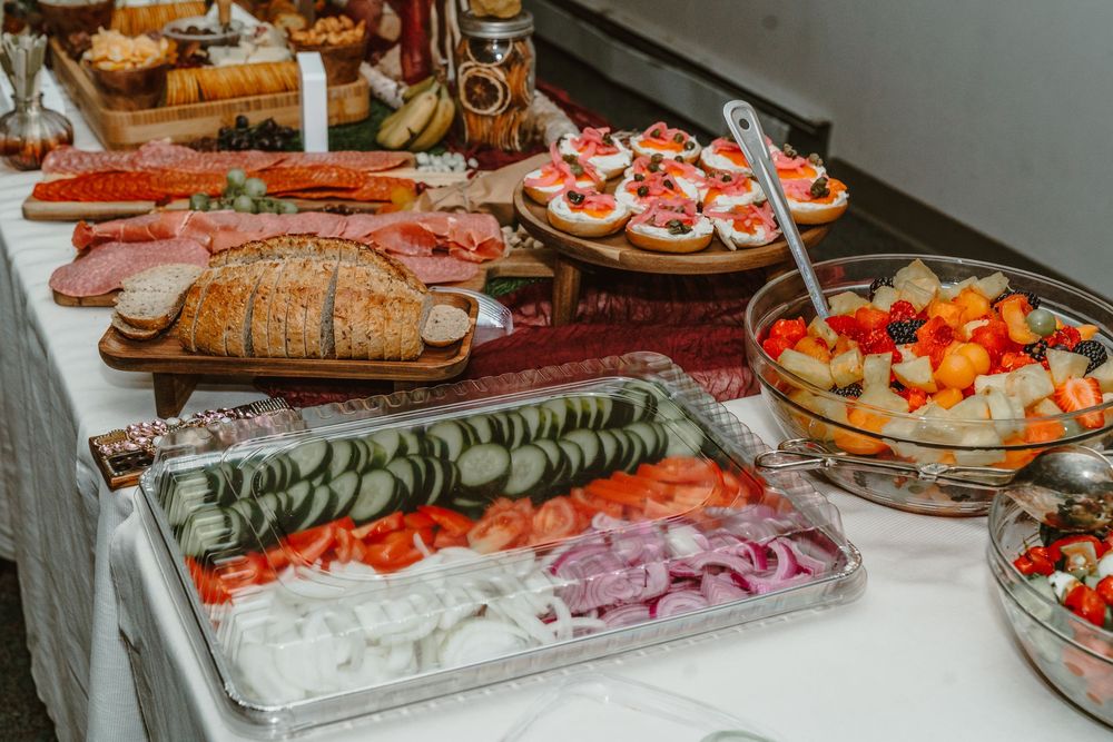 Elegant buffet table with sliced meats, fresh vegetables, fruit salad, and appetizers for a catered event.
