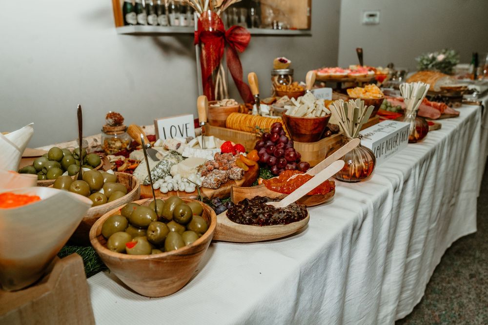 Elegant charcuterie grazing table with olives, cheeses, meats, fruits, and breads on white linen at a catered event.
