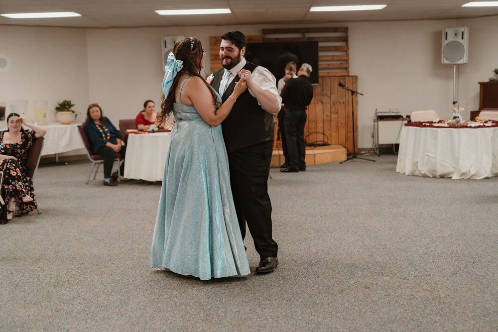 Couple sharing first dance at wedding reception, bride in light blue gown, groom in black suit, guests seated nearby.