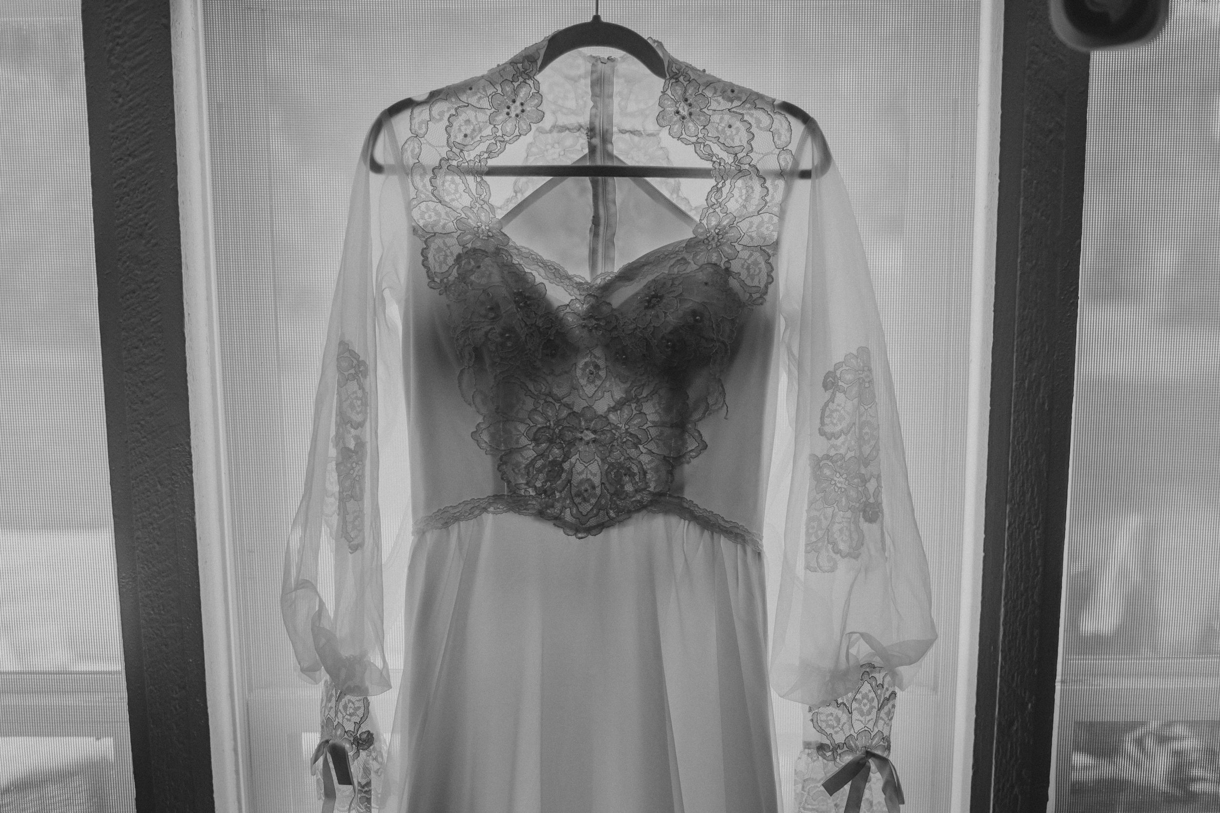 A vintage-inspired wedding dress with lace details and sheer long sleeves hangs elegantly on a hanger.