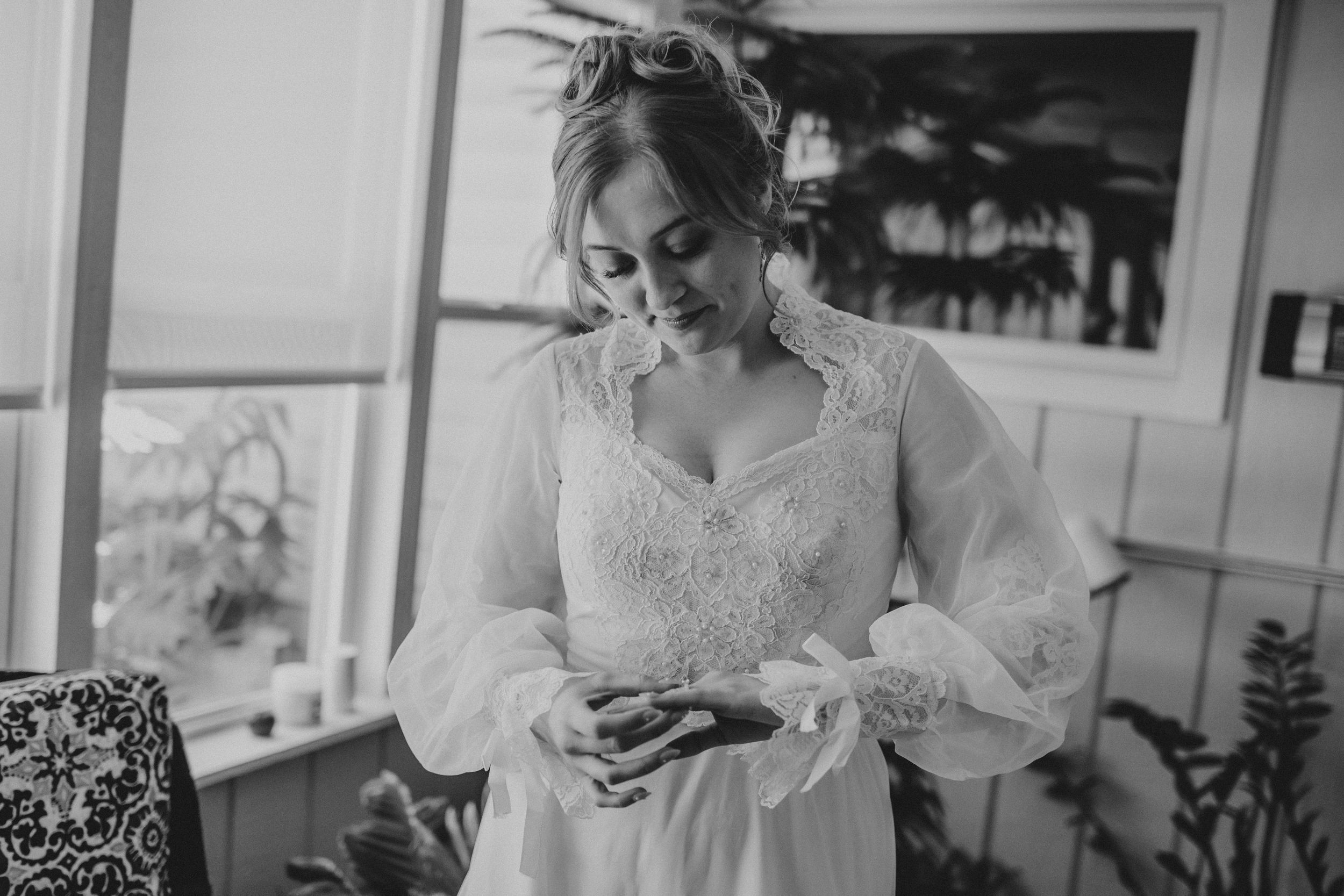 A black and white photo shows a bride in a lace dress with puff sleeves looking down at her phone.