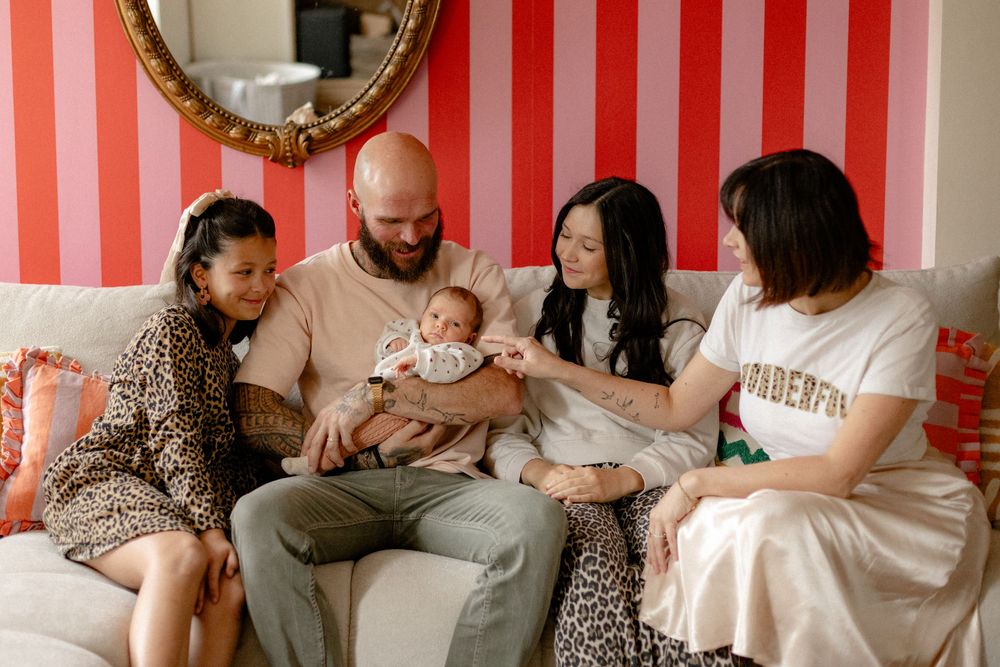 A family sits together on a couch in a room with red and white striped walls and a decorative mirror.