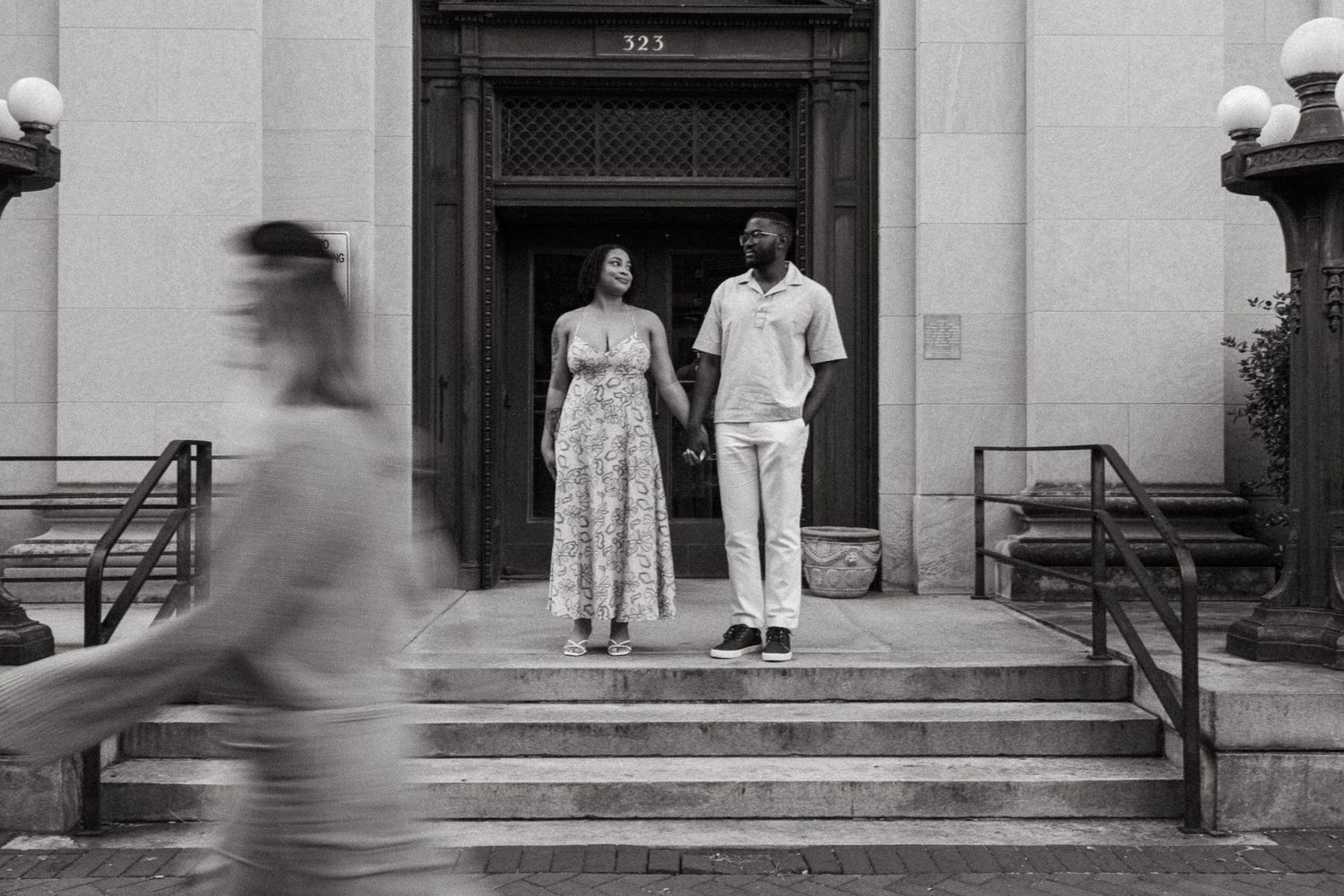 People in motion blur walk past and stand on the steps of a classical stone building entrance.