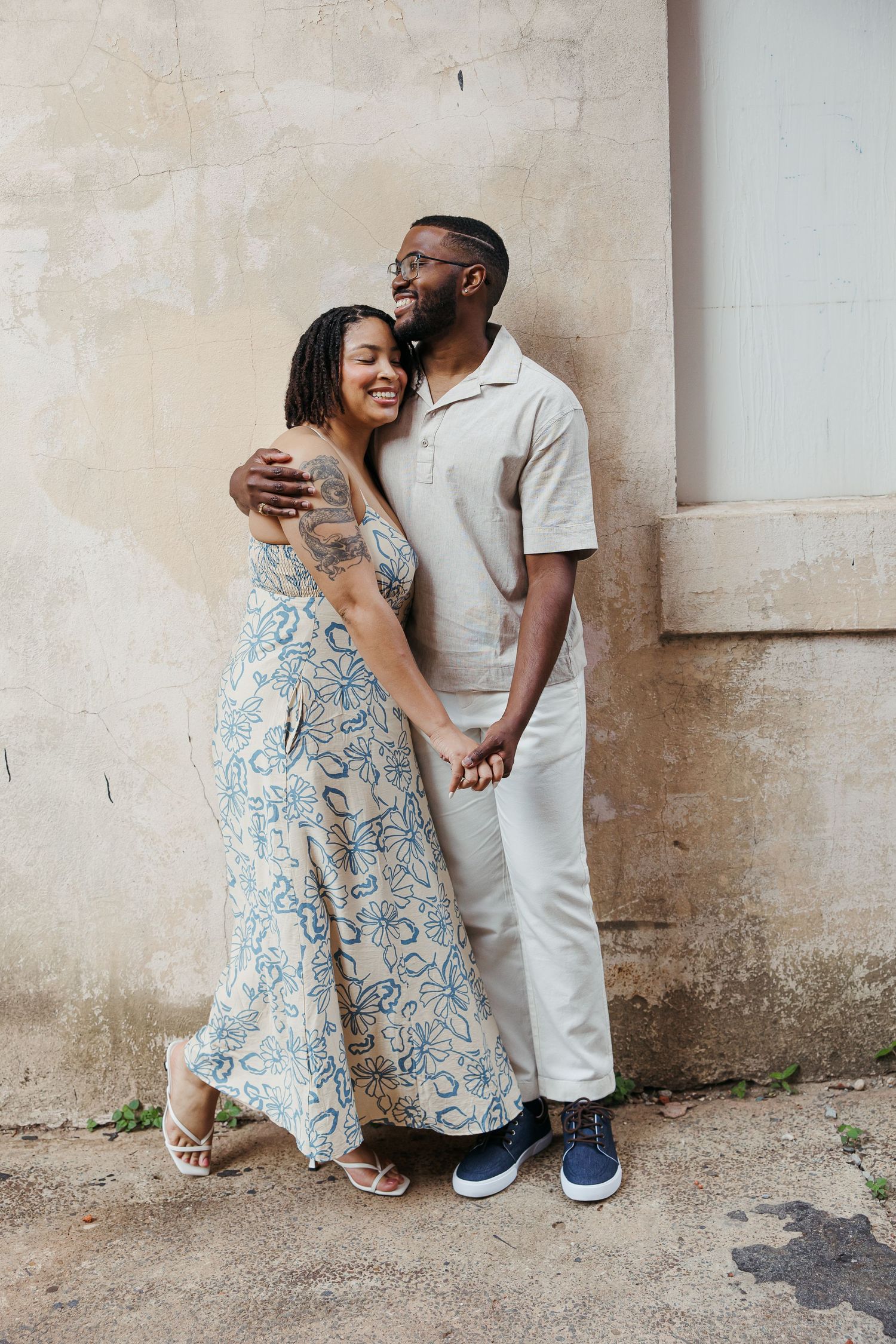 A couple shares intimate moments against a textured wall in a romantic outdoor photo series.