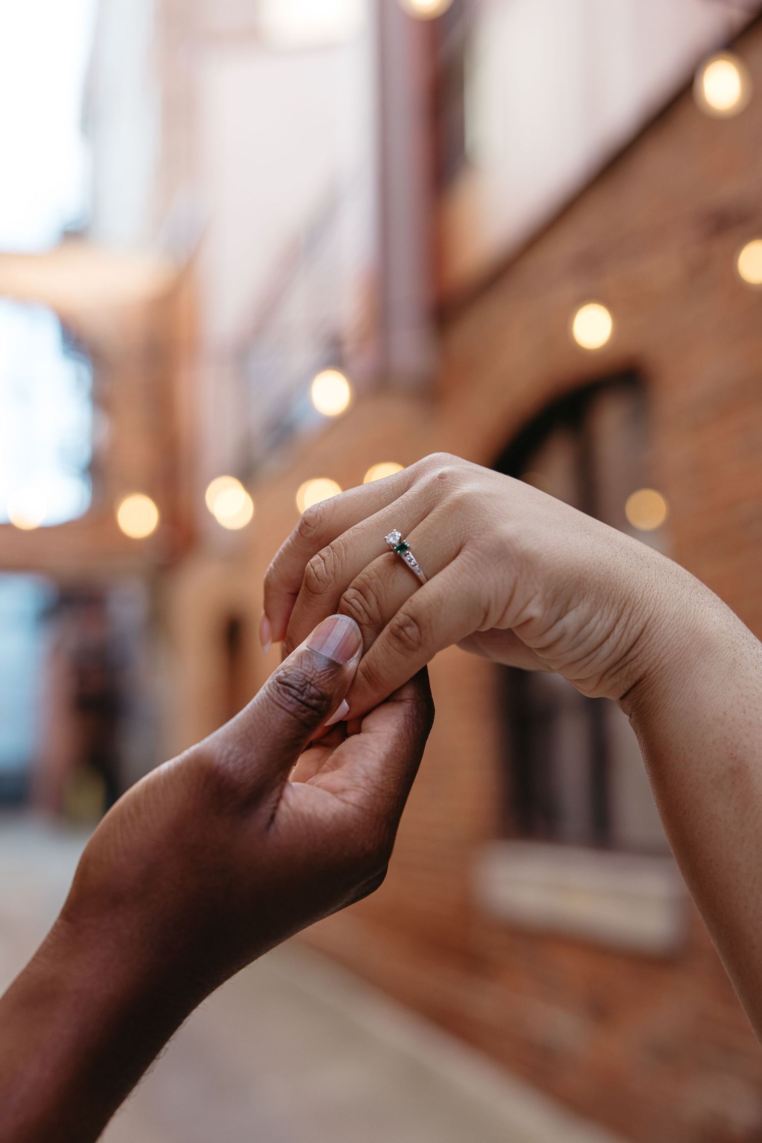 Close-up view of hands exchanging rings during a wedding ceremony with soft bokeh lights in the background.