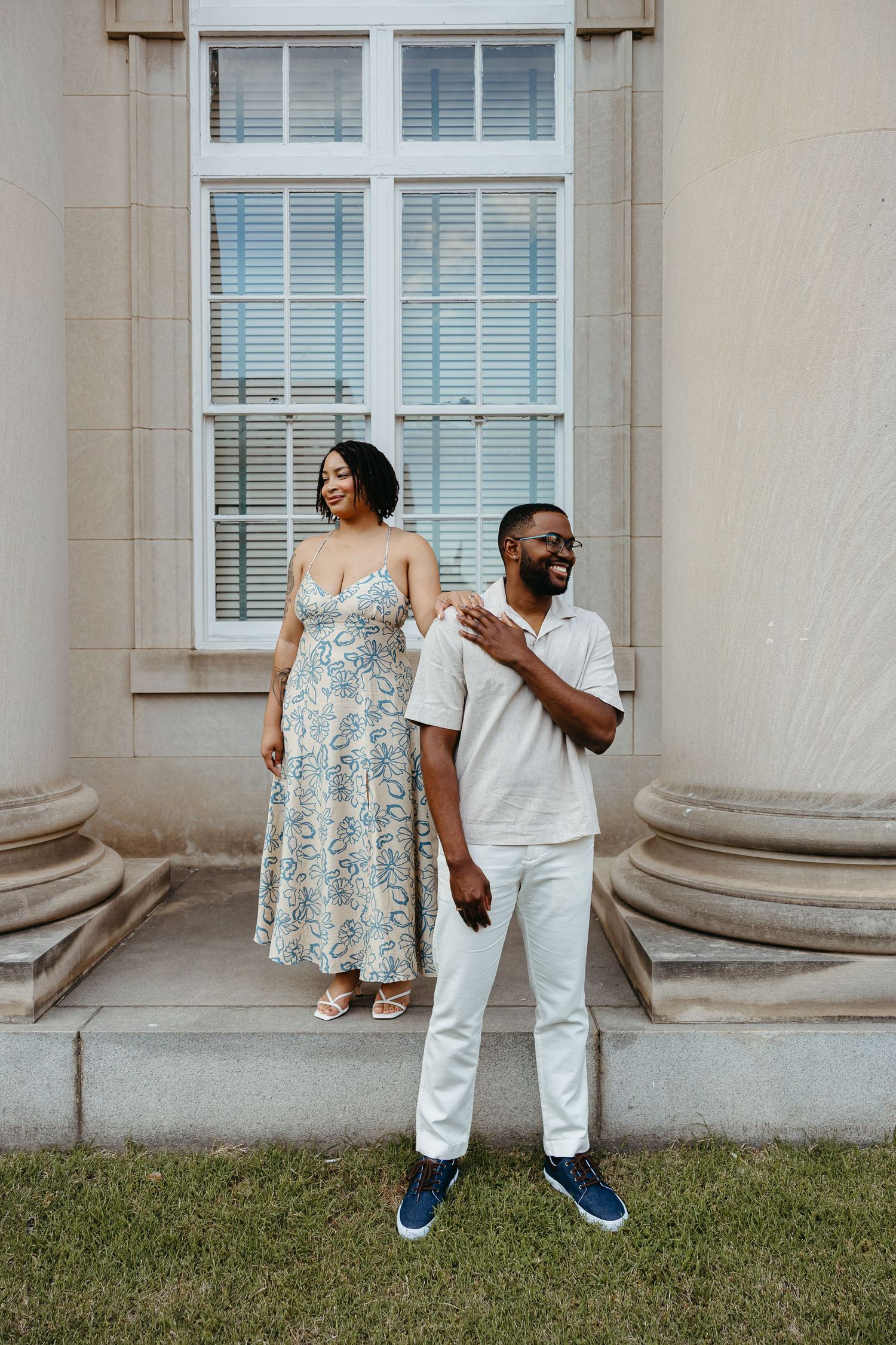 A couple shares a playful moment dancing together on a grassy lawn in front of a columned building.