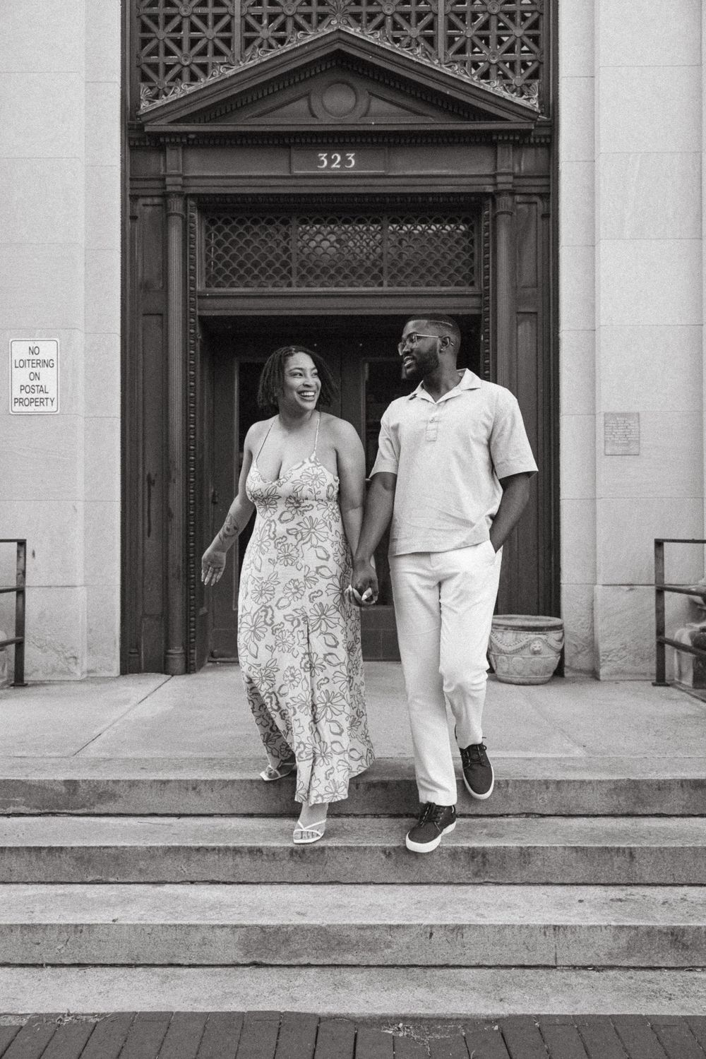 A couple in white clothing walks together along a historic building facade with ornate architectural details.