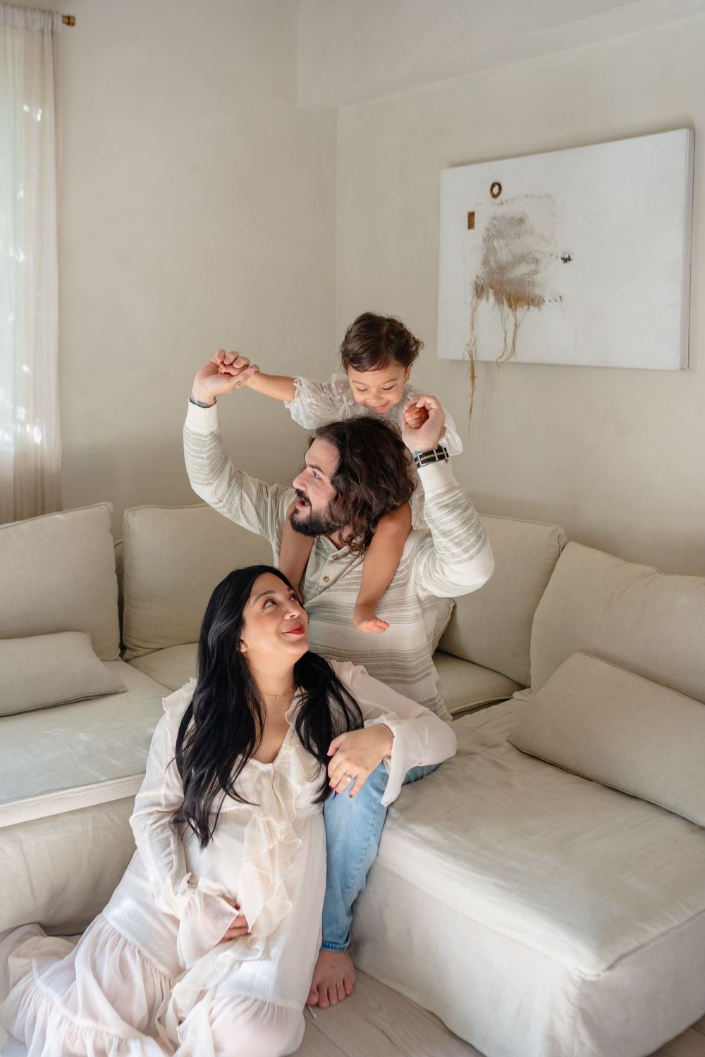 A couple relaxes and plays together on a white couch in a bright, minimalist living room setting.