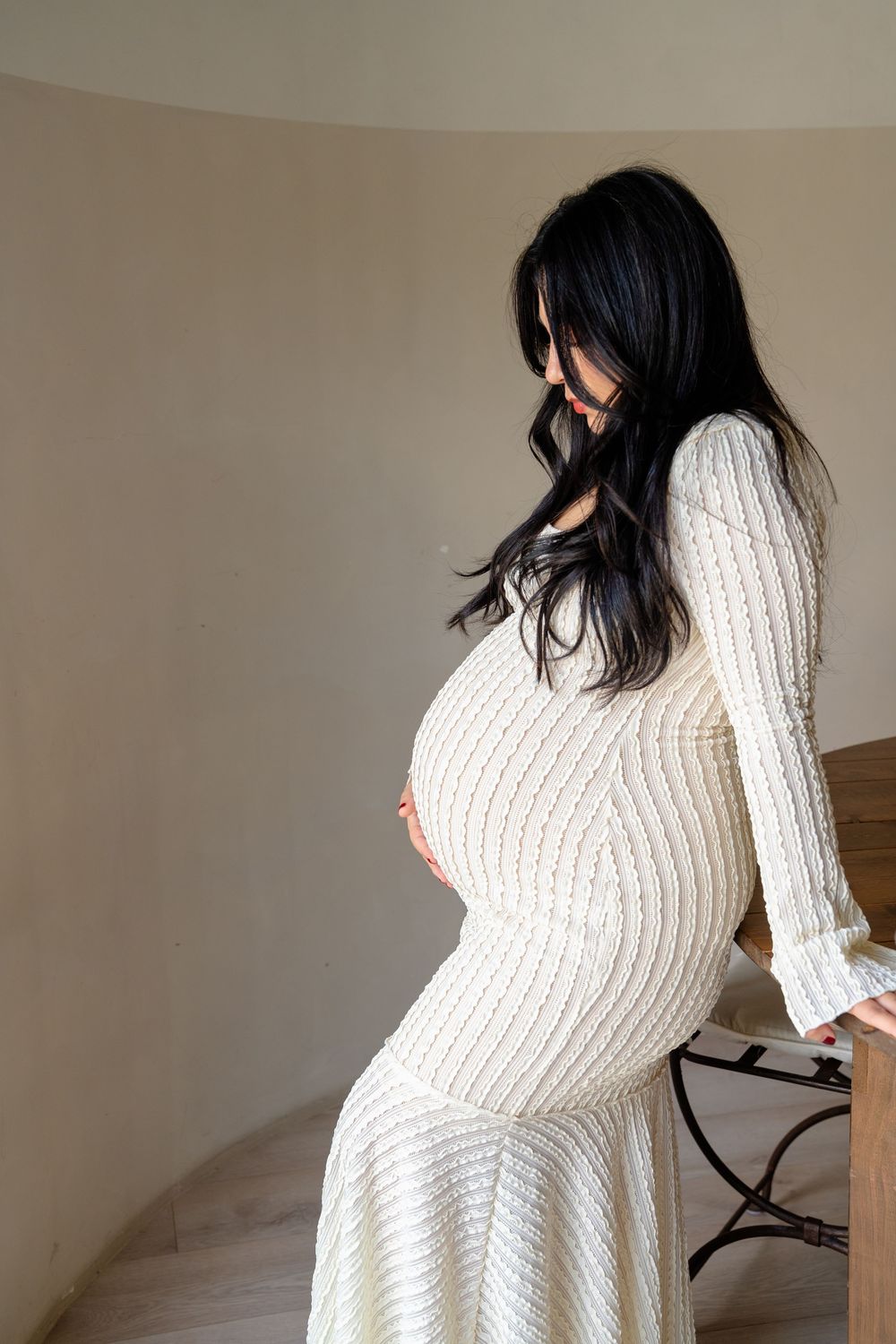 A person in a white ribbed sweater dress poses against a neutral wall.