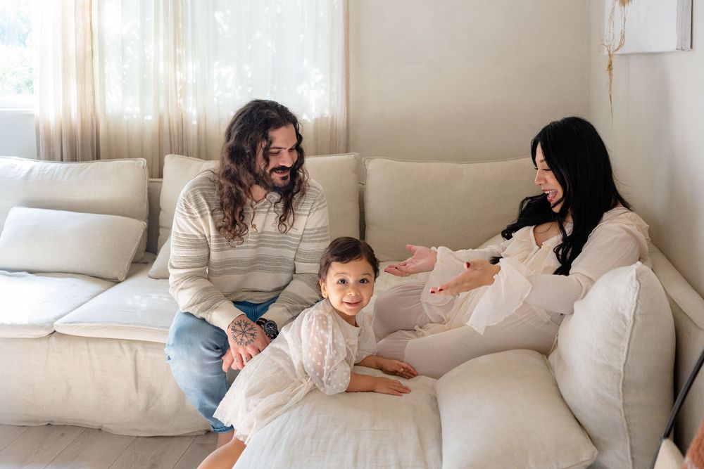 Family relaxes together on a comfortable white sectional sofa in a bright living room.