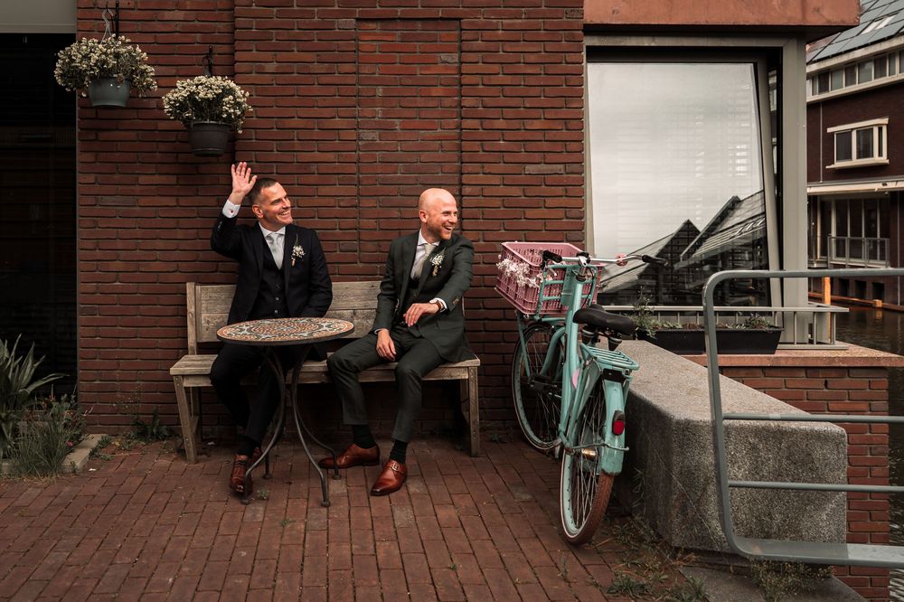 People sitting and standing outside a brick building with steps and railings.