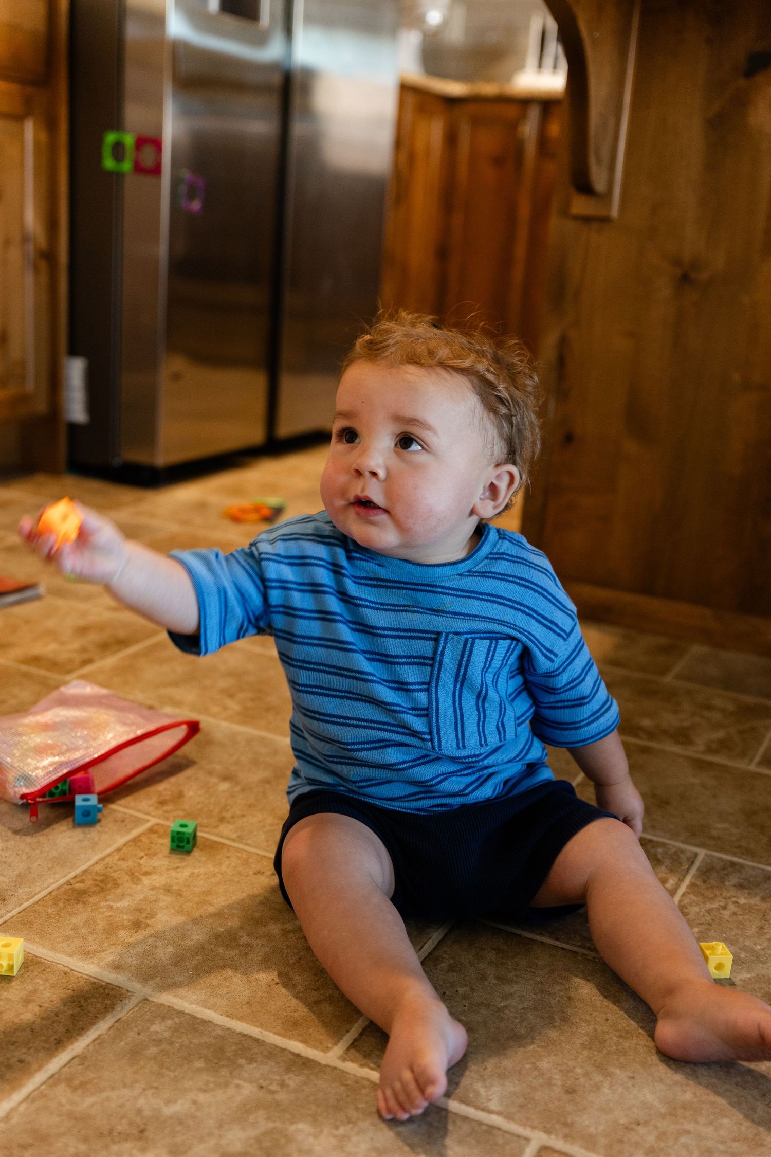 1 year old sitting on floor in a blue shirt handing mom a toy