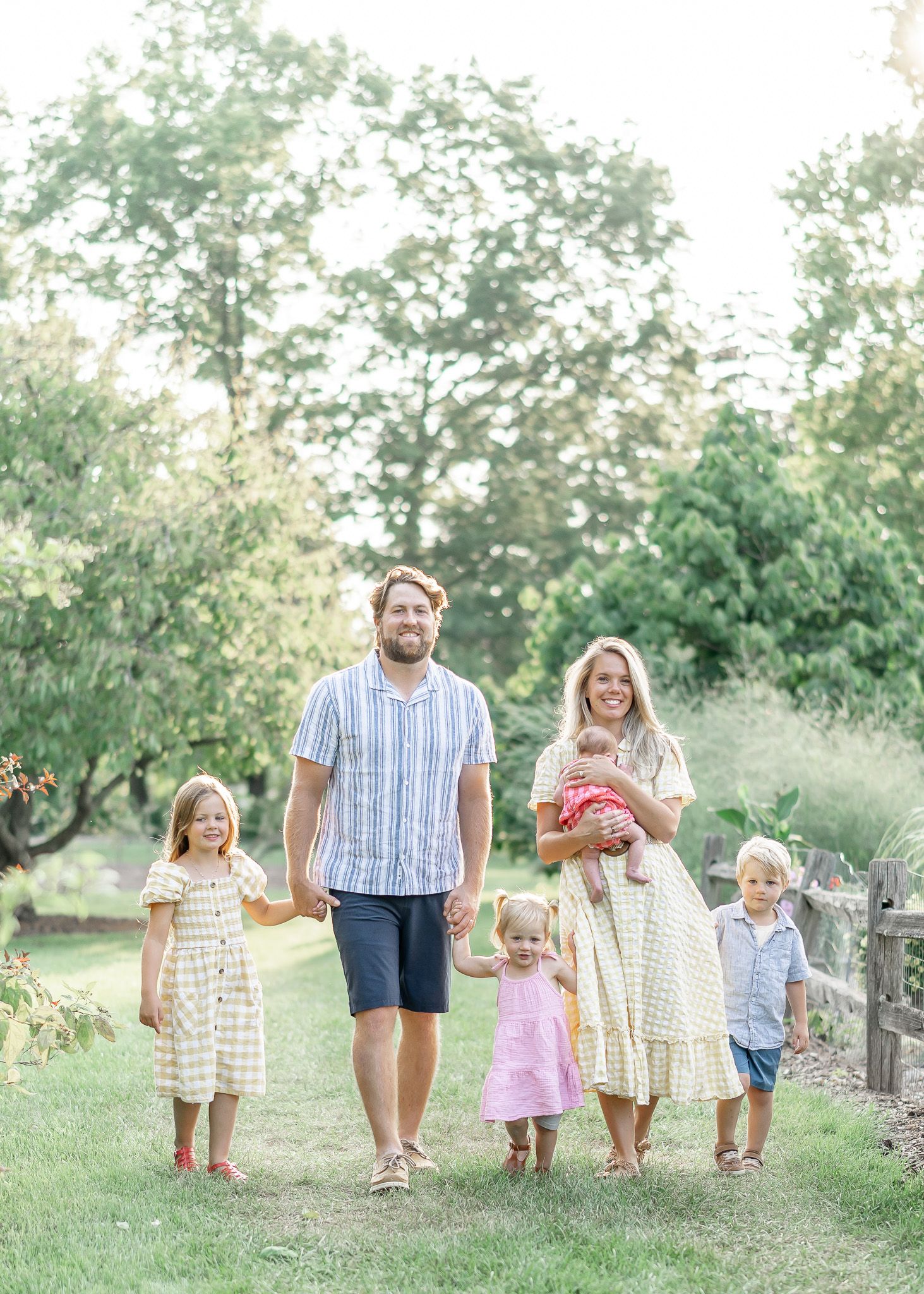 Family walking together in a grassy outdoor setting wearing coordinated neutral colored outfits.