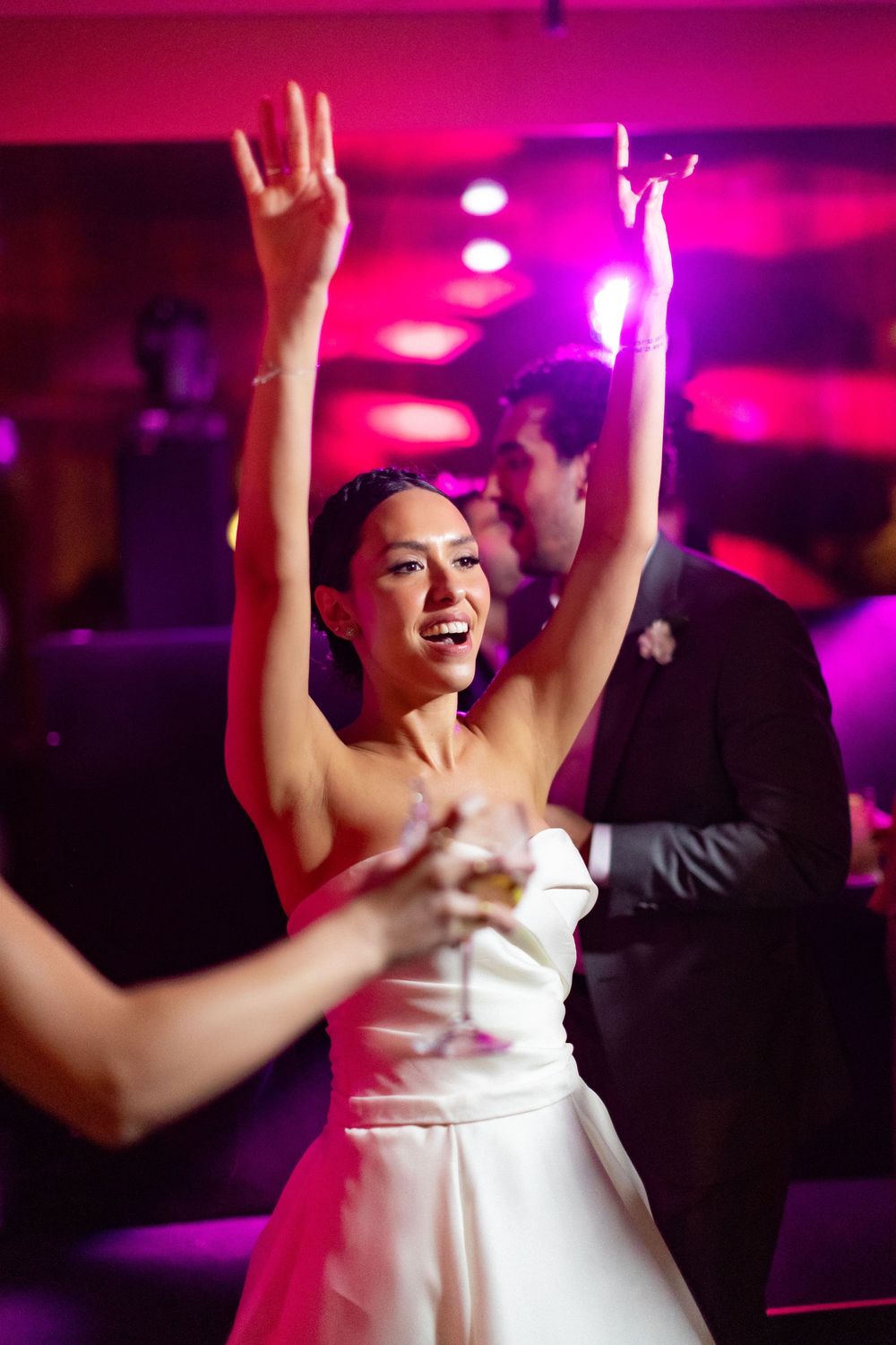 A person in a white dress dances joyfully under vibrant pink nightclub lighting.