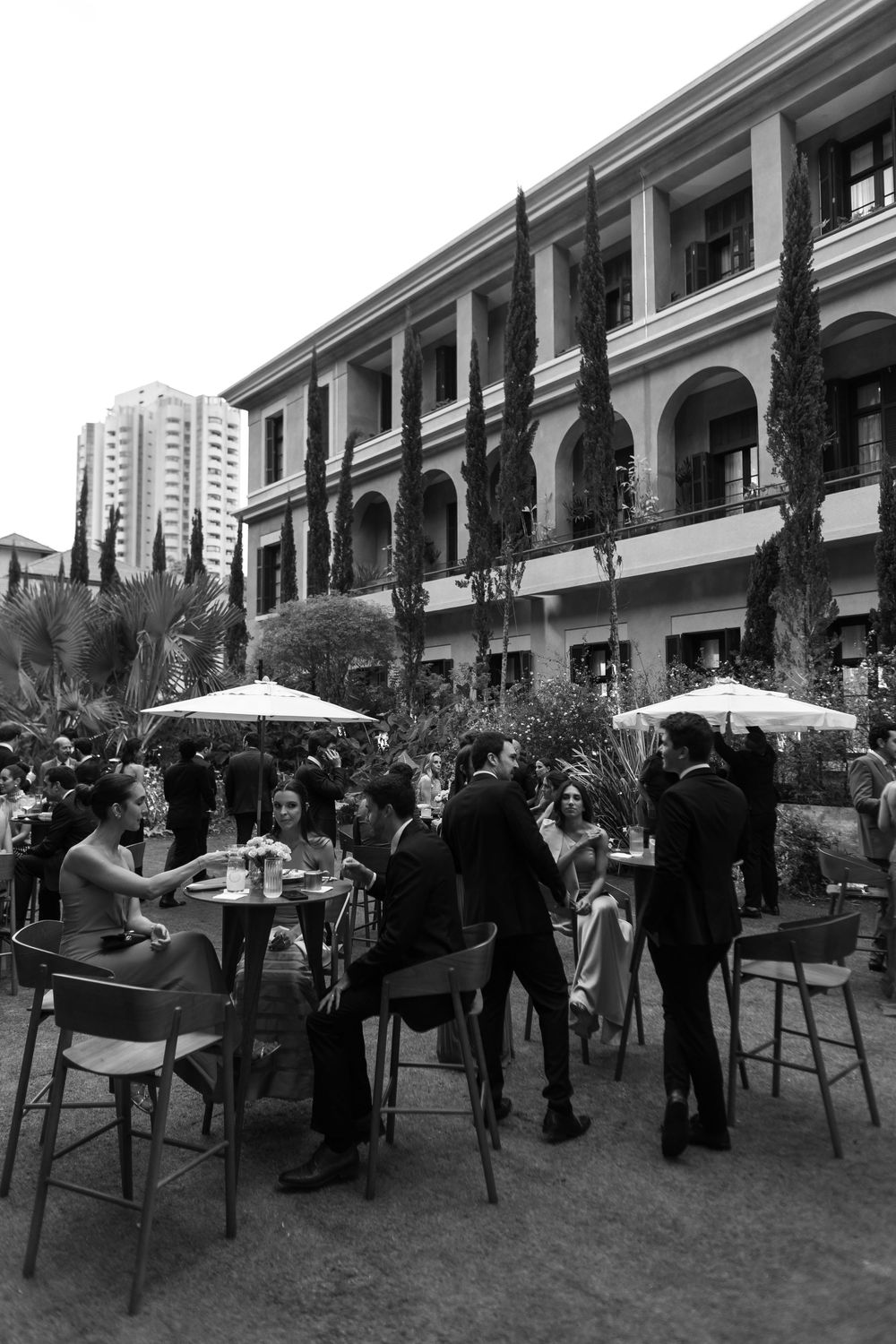 Outdoor courtyard gathering with tables, umbrellas and guests mingling in black and white.