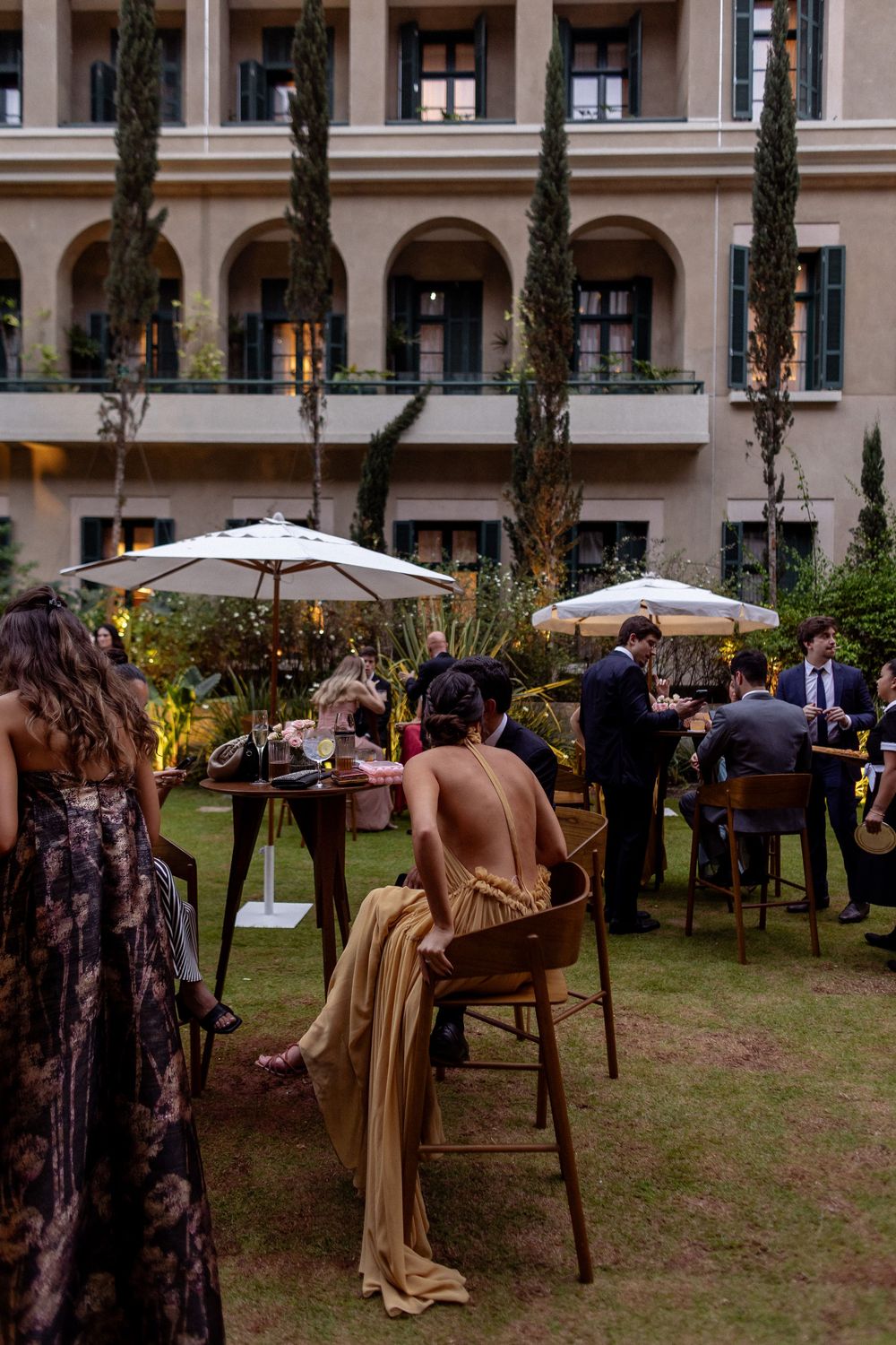 Wedding guests enjoy an elegant outdoor reception with umbrellas and tables set up on a lawn.
