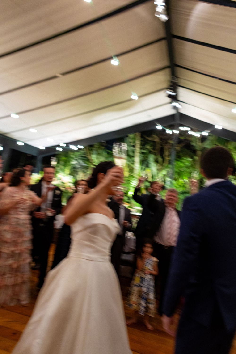 Wedding guests dance together during a lively reception celebration under warm indoor lighting.