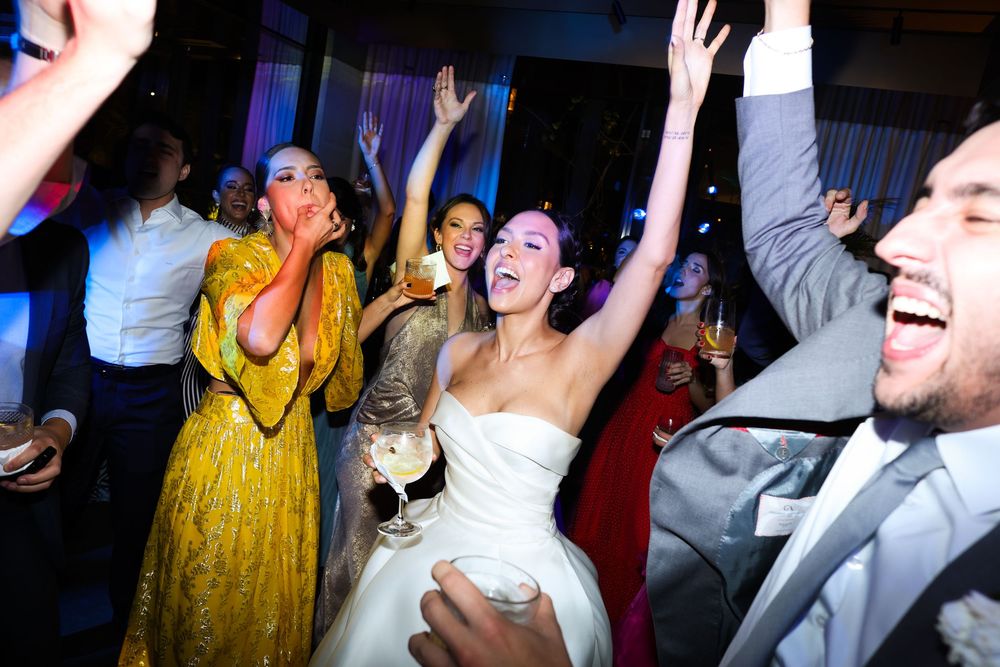 Joyful party guests dancing and raising their hands on a dimly lit dance floor.