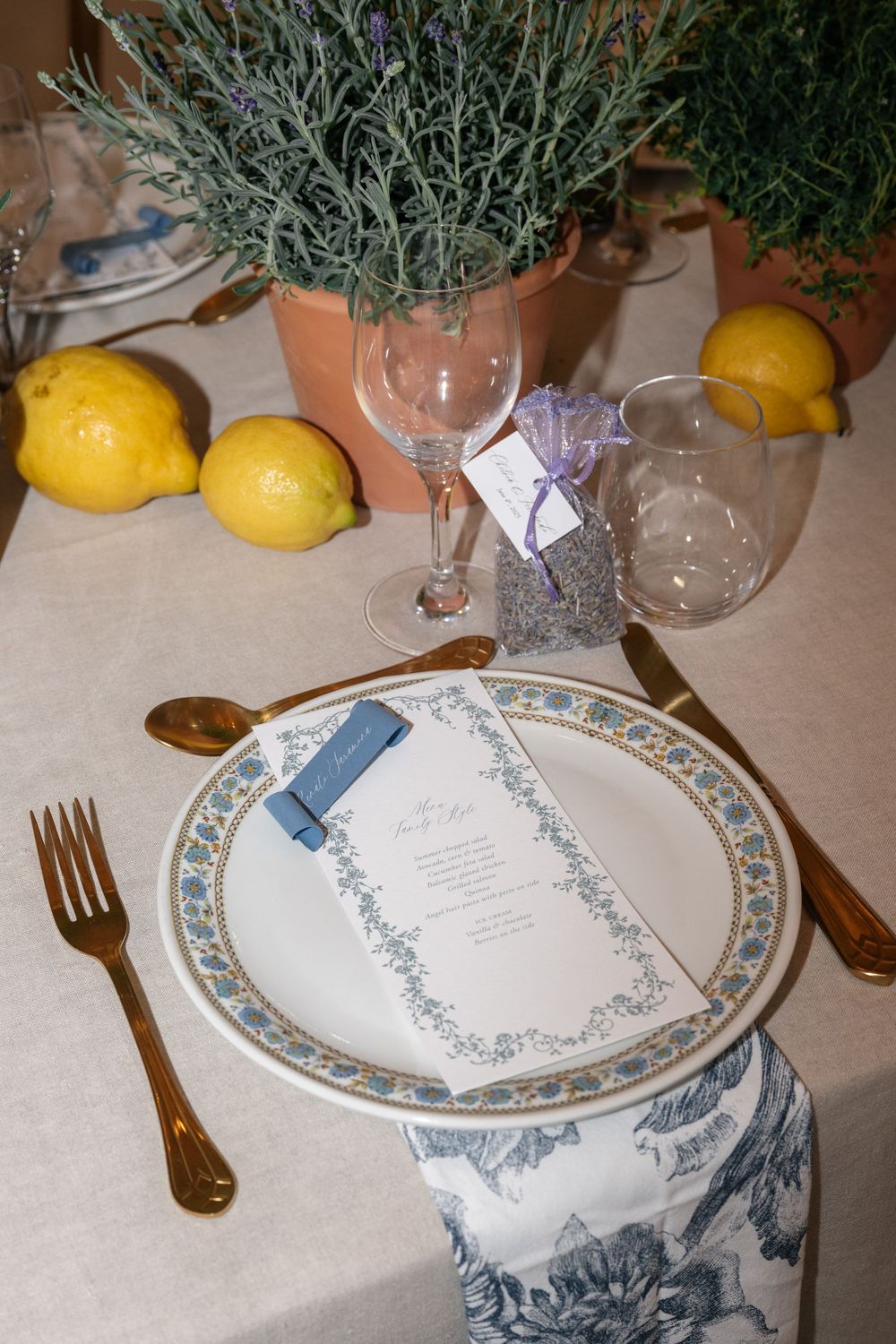 Place settings with decorative plates, lemons, and lavender sprigs on a cream-colored tablecloth create an elegant dining scene.