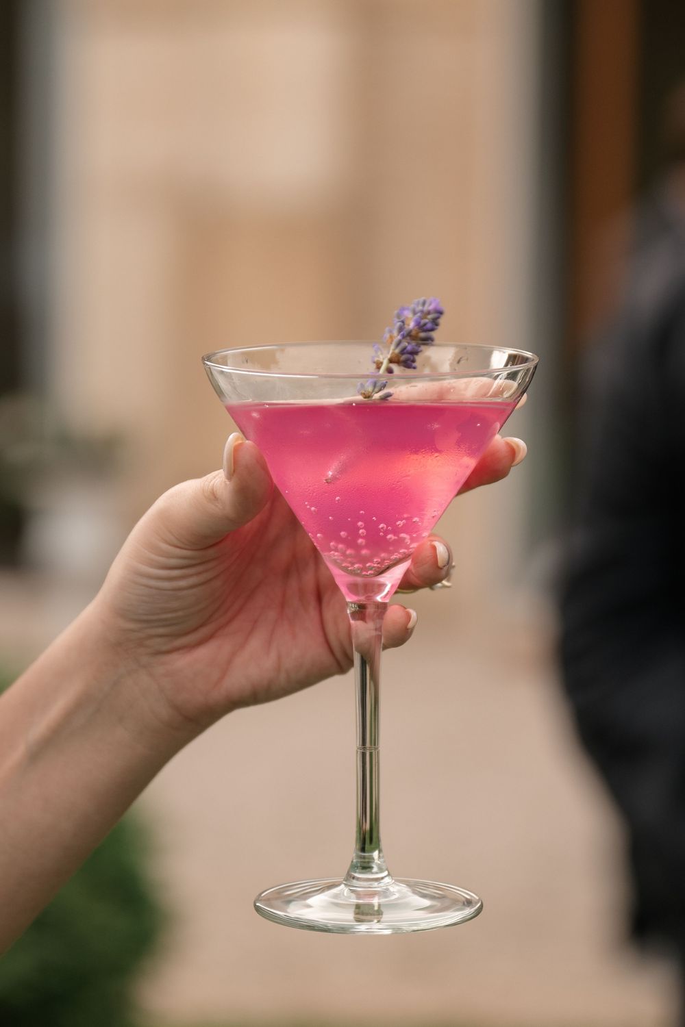 Four identical pink cocktails in martini glasses garnished with lavender sprigs against a blurred background.