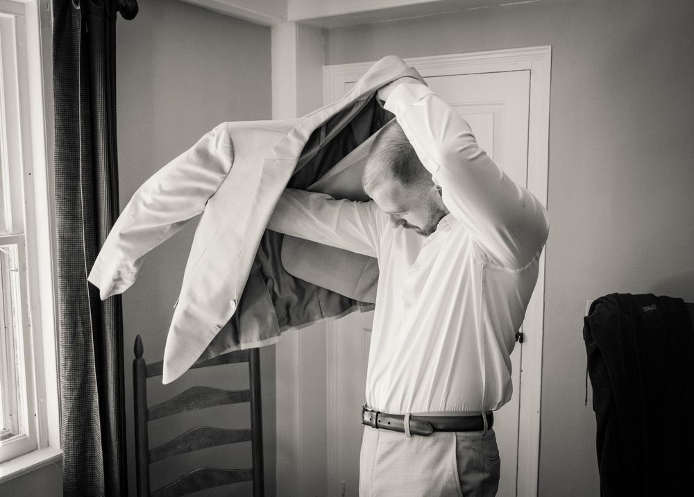 Man putting on suit jacket in black and white wedding preparation photo.