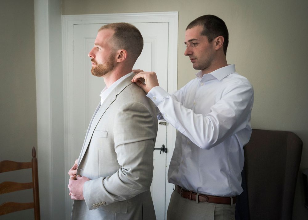 Groomsman helping groom adjust suit jacket collar before wedding ceremony.