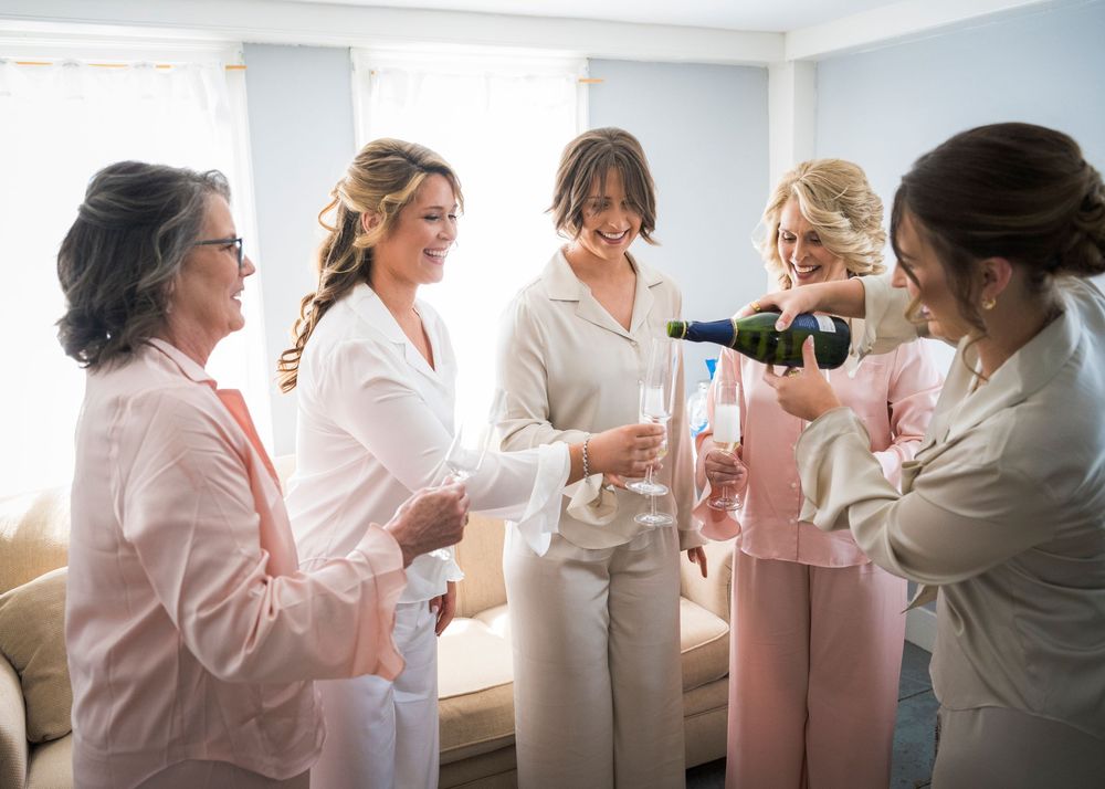Bridesmaids in robes celebrate with champagne toast during bridal party getting ready before the wedding.