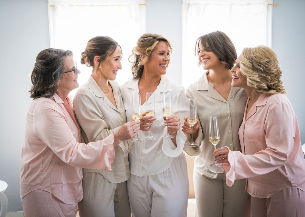 Bride and bridesmaids toasting with champagne in matching satin pajamas before the wedding.