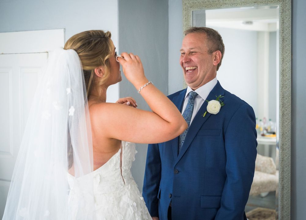 Smiling groom in navy suit shares a joyful moment with bride in white wedding dress and veil before ceremony.