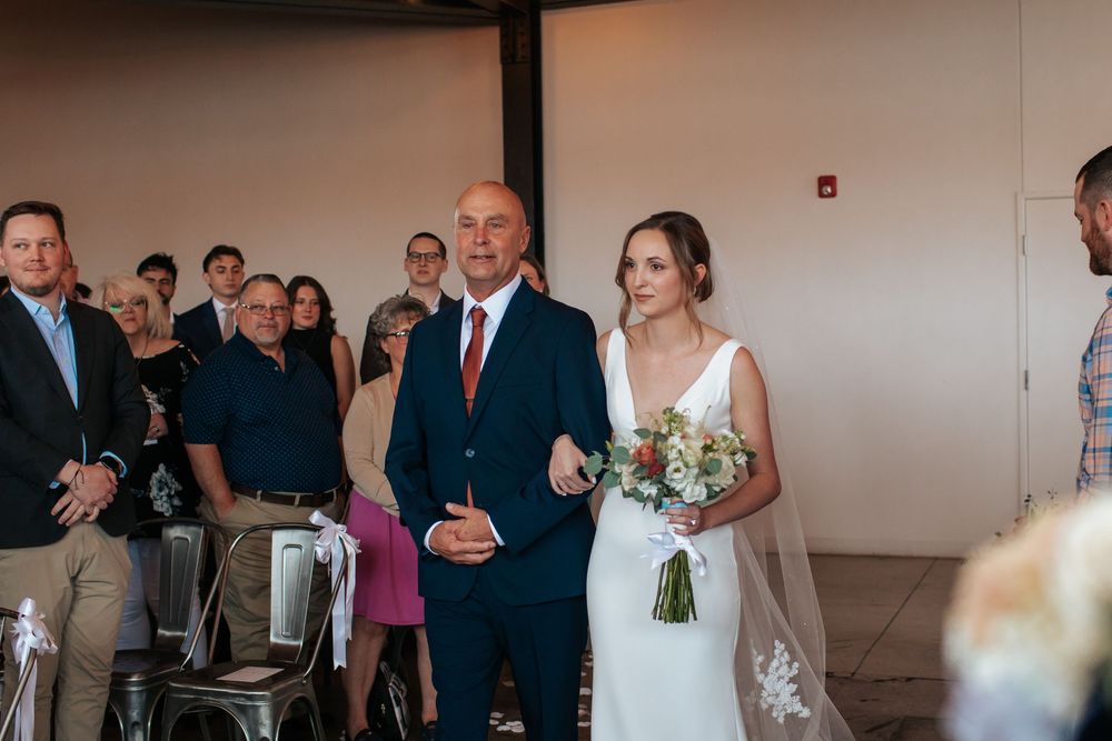 Wedding party gathers in an elegant reception hall with white floral arrangements and formal attire.