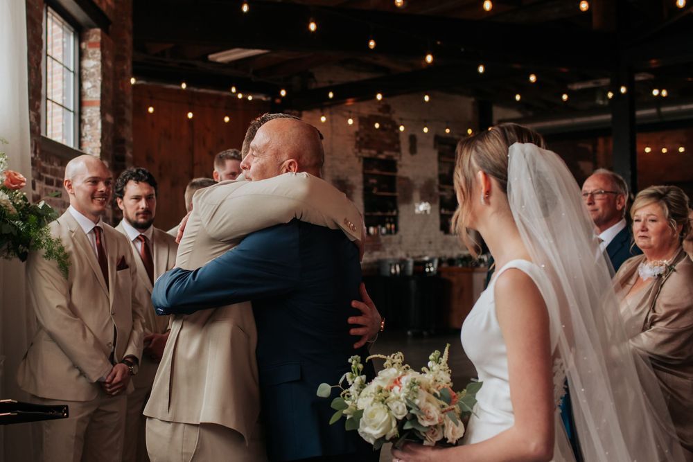 An emotional moment during a wedding ceremony in a rustic venue decorated with string lights.