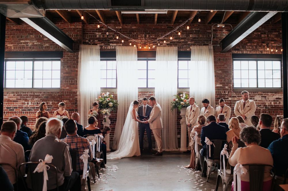 Wedding ceremony in a rustic brick venue with exposed beams and string lights illuminating the industrial space.