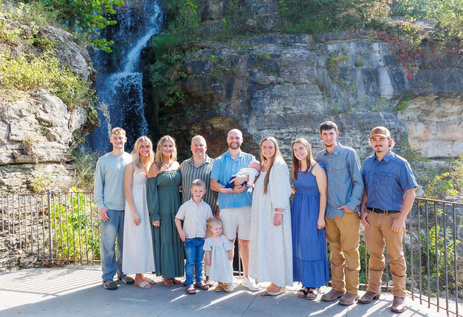 Group photo taken at a scenic waterfall overlook with stone walls and lush greenery in the background.