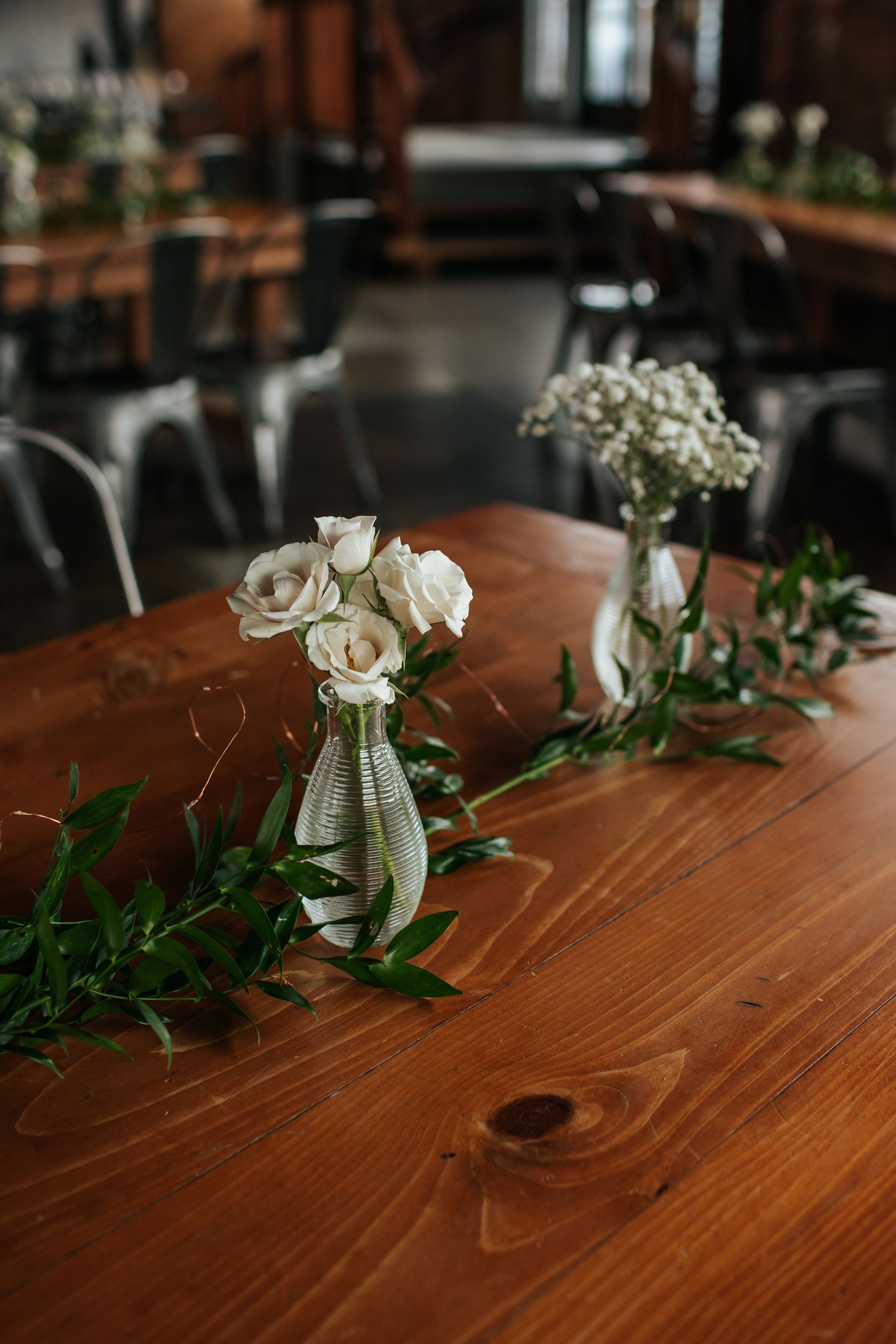 White roses and baby's breath in simple vases create an elegant table setting on a rustic wooden surface.