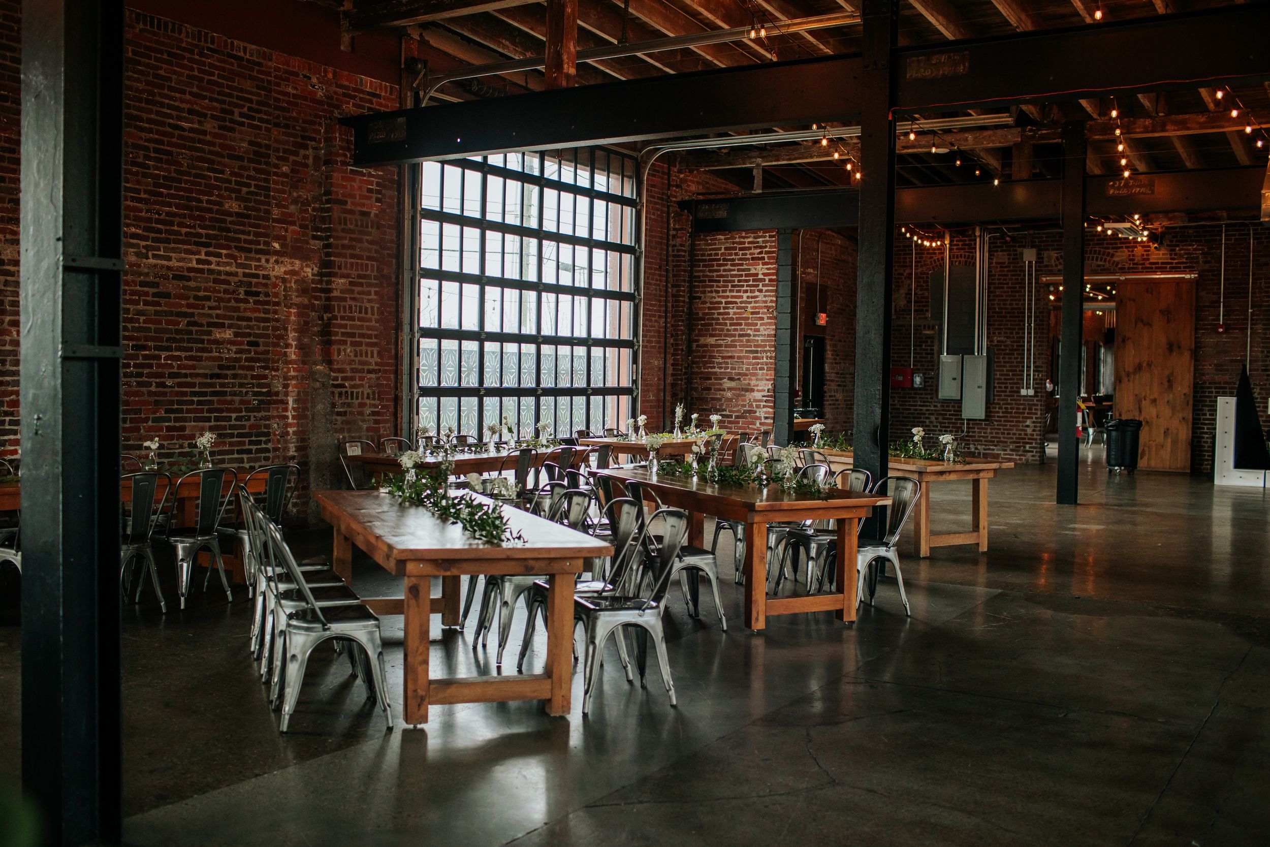 Industrial loft restaurant with exposed brick walls, large windows, and metal chairs in a rustic-modern setting.