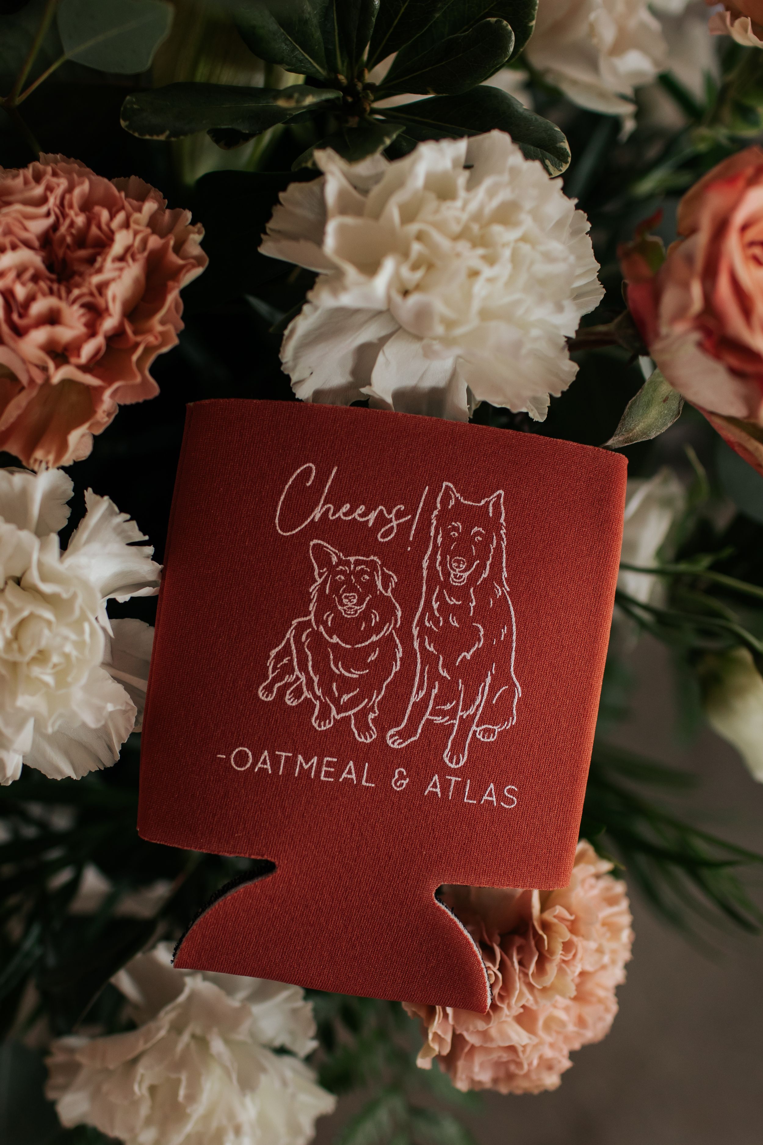 Three burgundy business cards with whimsical animal illustrations displayed among pink and white carnations.