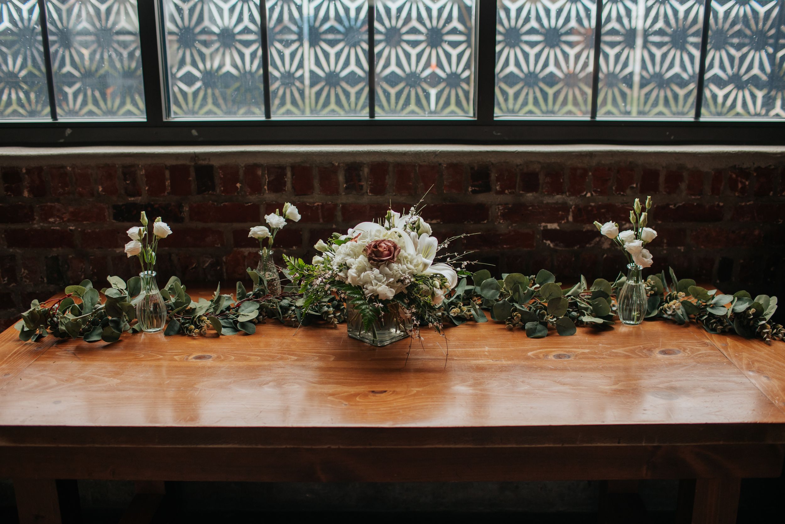 A series of floral arrangements with white flowers and greenery line the edge of a dark wooden stage or platform.