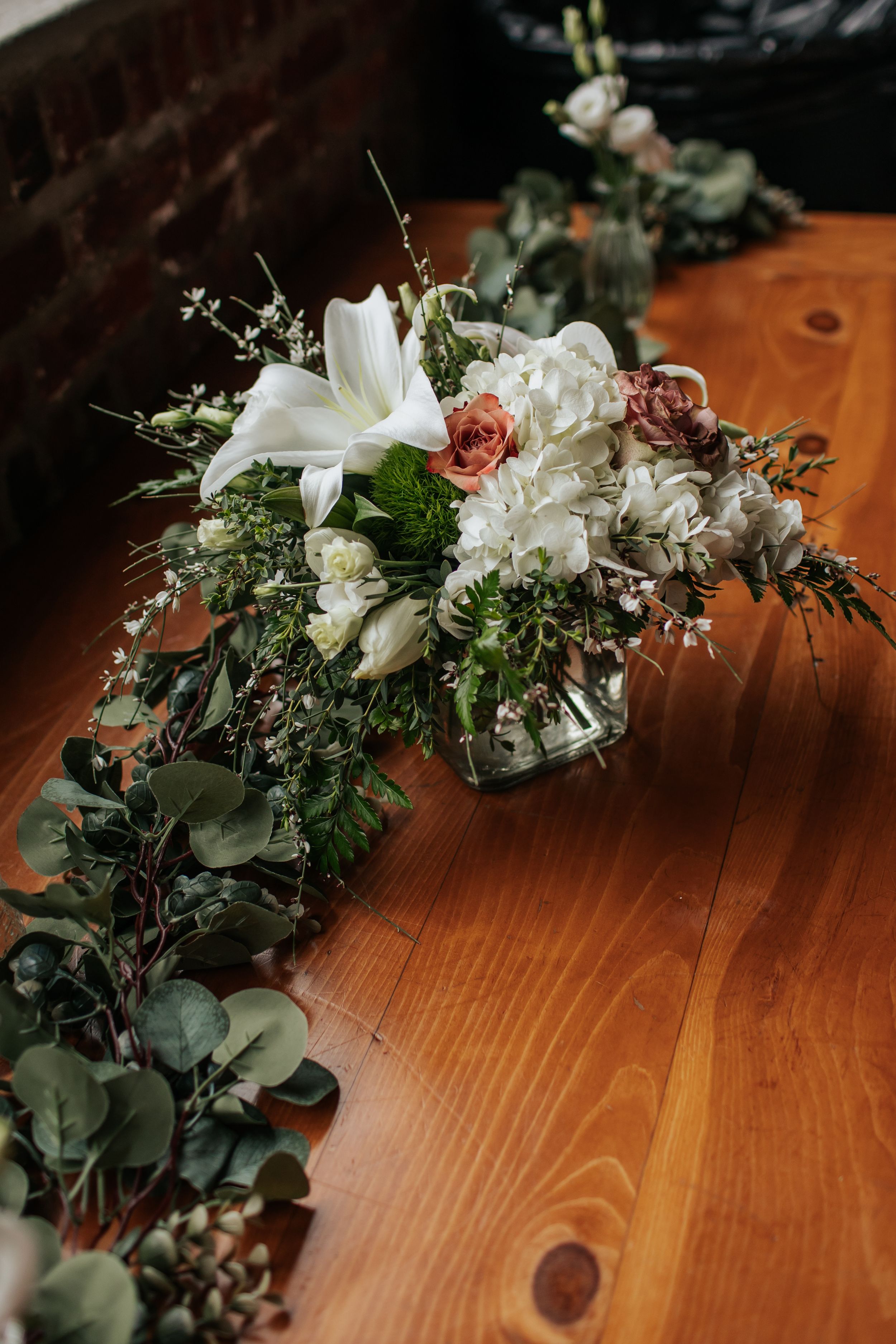 Elegant floral arrangement with white lilies, roses, and eucalyptus leaves on a wooden table.