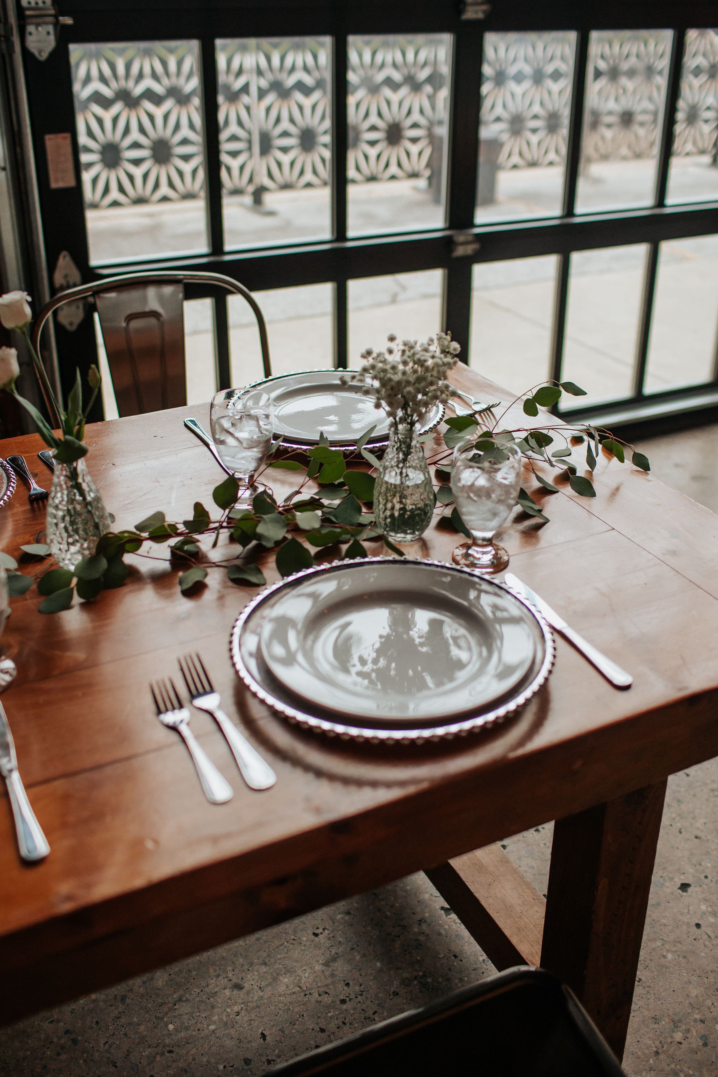 Elegant table setting at a restaurant with ornate plates, silverware, and decorative greenery along a wooden table.