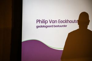 Een silhouet van een spreker voor een projectiescherm met de tekst "Philip Van Eeckhoute - gedelegeerd bestuurder"