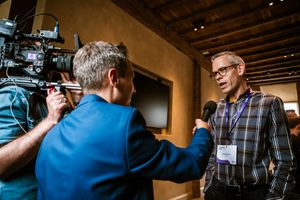 Een journalist interviewt een deelnemer met een microfoon, terwijl een cameraman het moment vastlegt tijdens een event