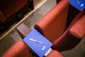 Blauwe notitieboeken met het logo van Liantis en pennen liggen op rode theaterstoelen, klaar voor een conferentie.