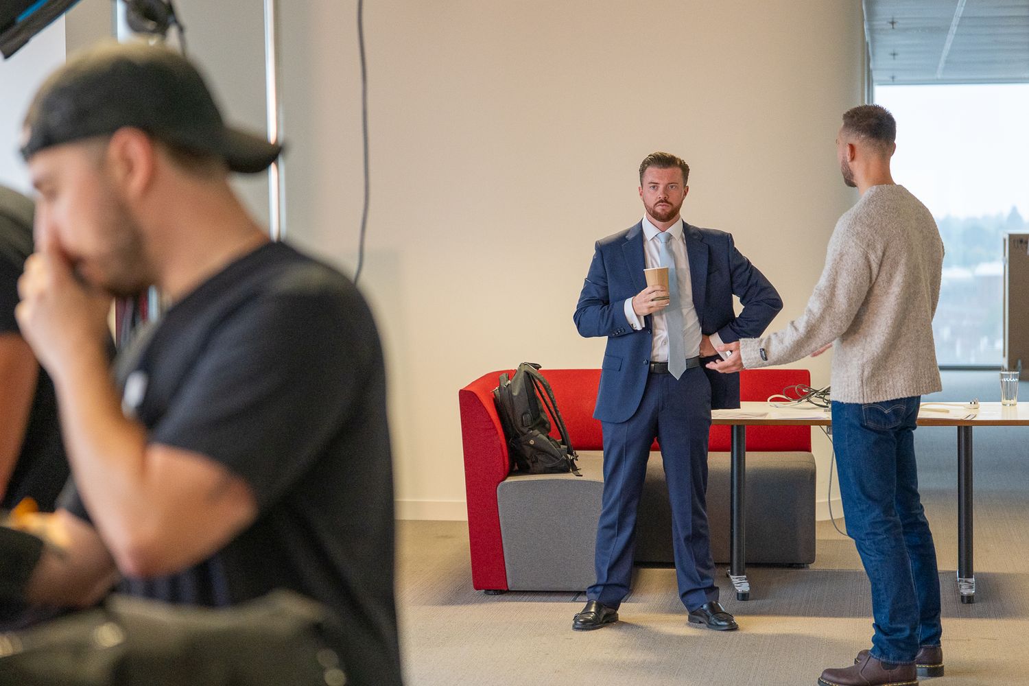 Business professionals having a casual conversation in a modern office space with red furniture and bright lighting.