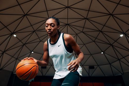 Basketball player dribbling on indoor court wearing white jersey during intense practice session.
